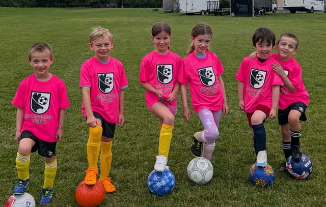 Six young campers in pink shirts smiling, each with a foot on a soccer ball, Summer Camp 2026