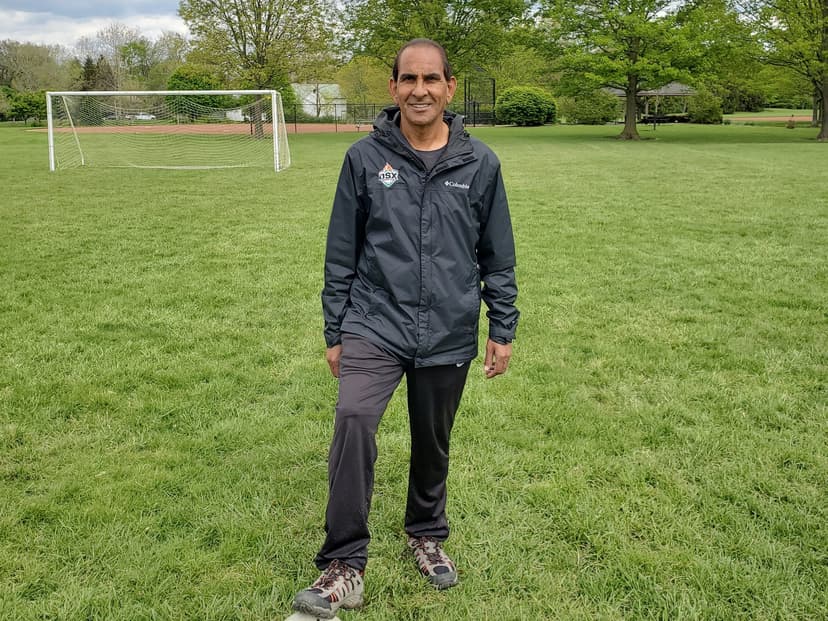 Coach Mo on a soccer field with his foot on a ball, a goal behind him